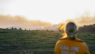 A Rural Fire Service Queensland volunteer stands with her back to the camera looking at a field