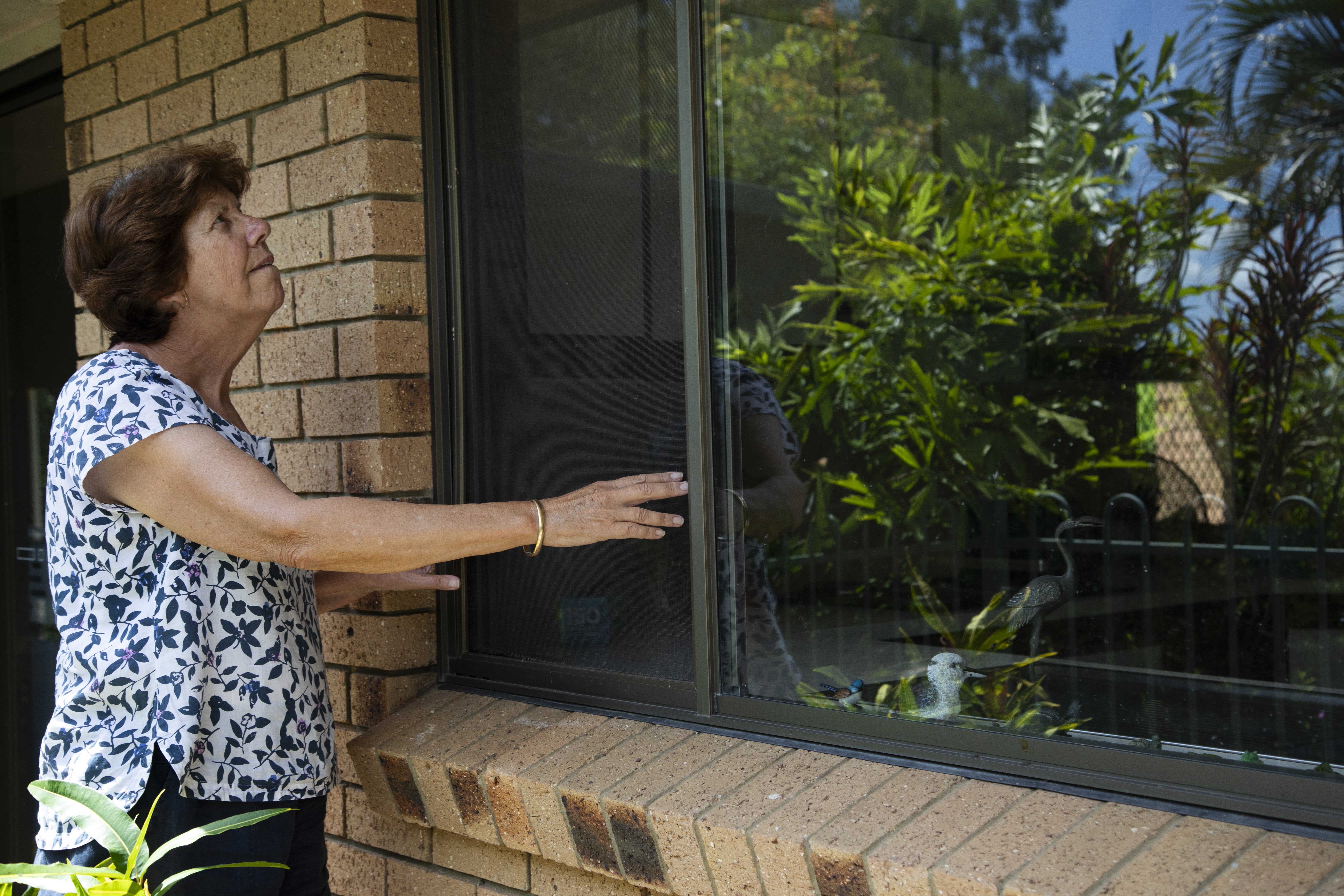 A woman stands outside her home inspecting her window