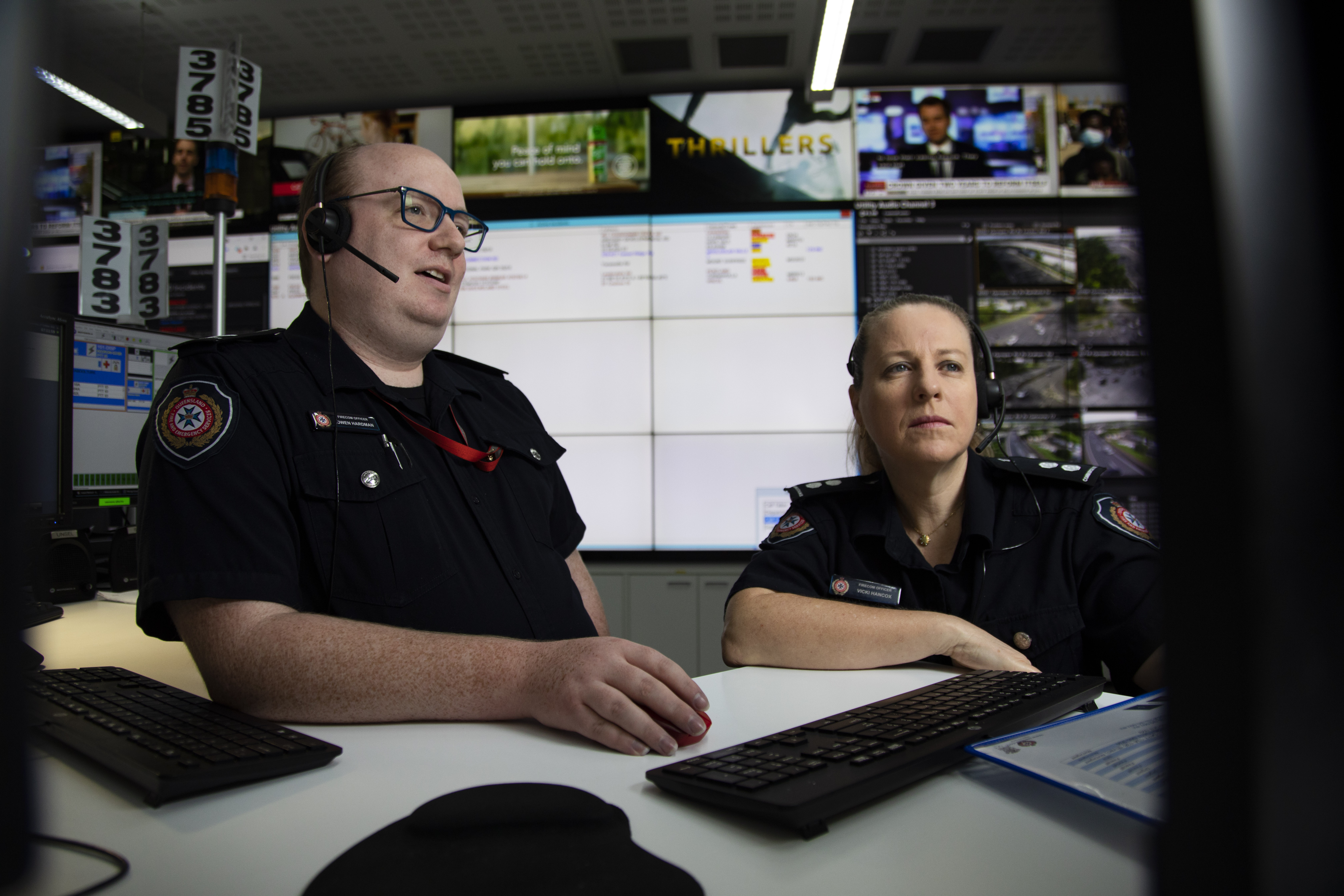A male and female FireCom officer sit as a desk facing the camera, looking at a computer screen off camera. 