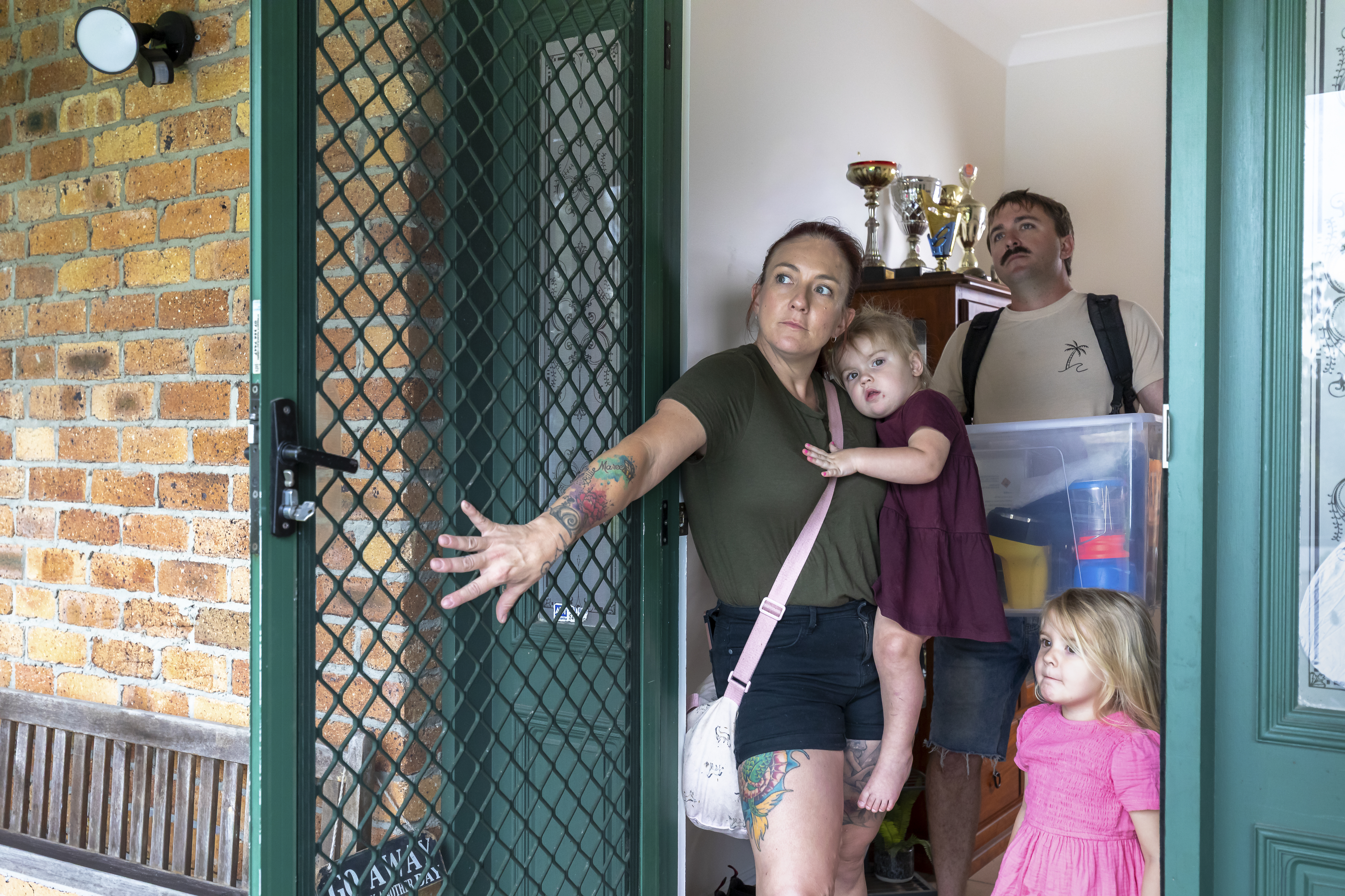 A family of two adults and two young children stand at their open front door with their emergency evacuation kit.